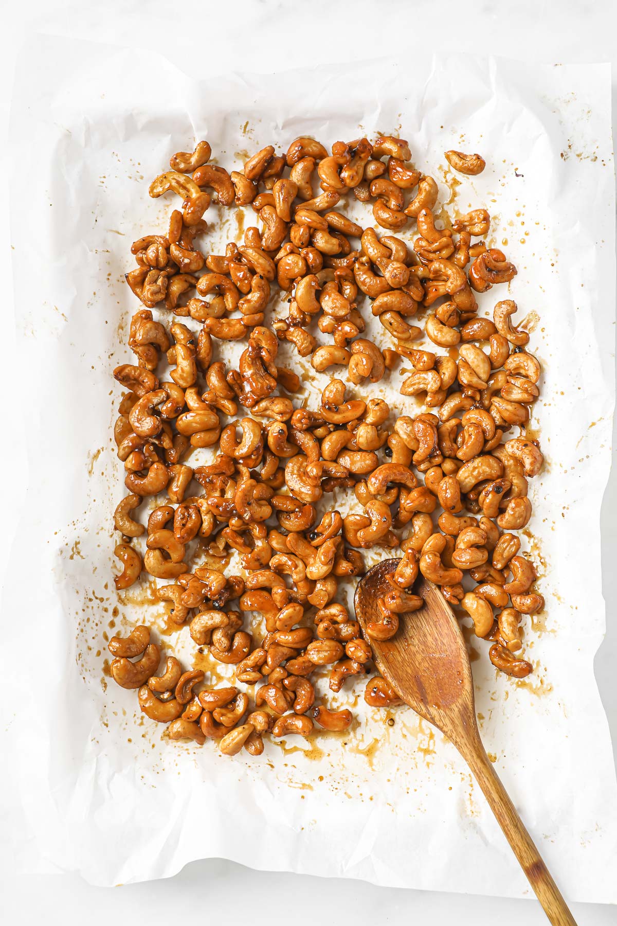 Roasted with honey cashews with wooden spoon on parchment lined baking pan.