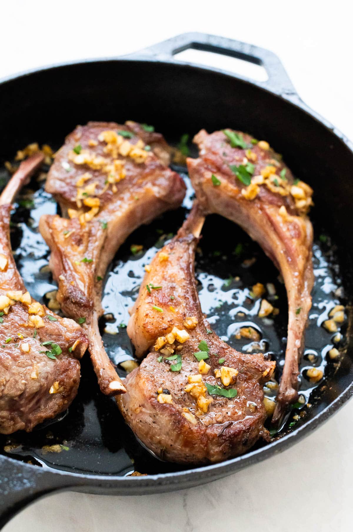Four pan fried lamb chops with garlic butter and parsley in cast iron skillet.