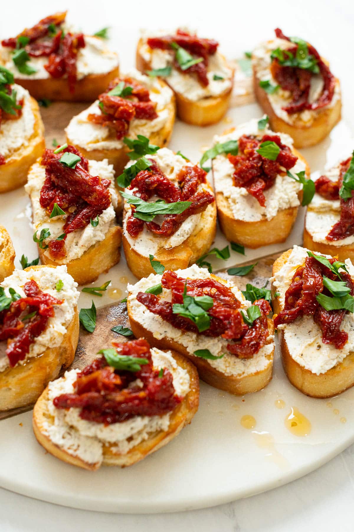 Crostini with goat cheese and sun dried tomatoes and parsley on marble platter.