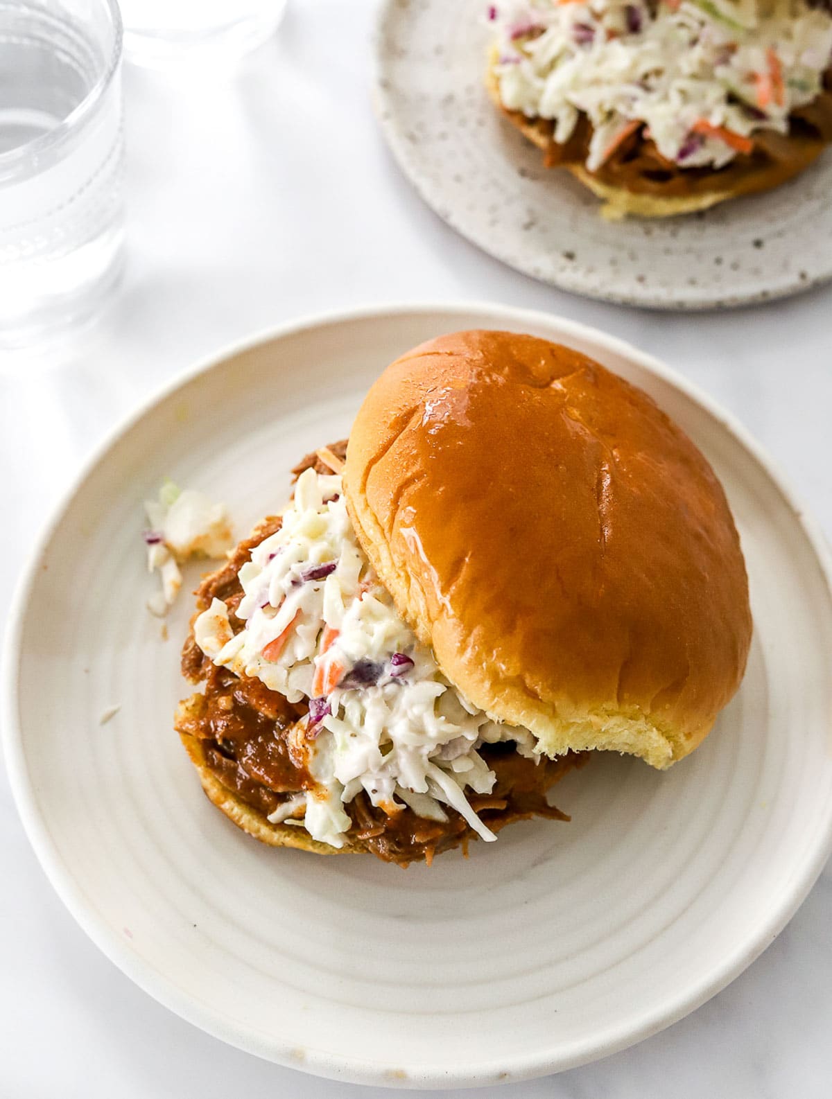 Pulled pork sandwich on brioche bun with coleslaw on white plate.