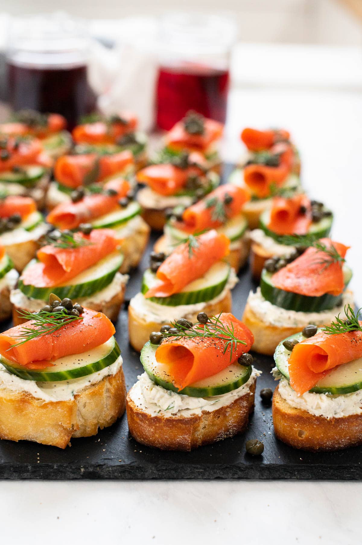 Salmon appetizers with cream cheese, cucumber, capers and dill on black platter.