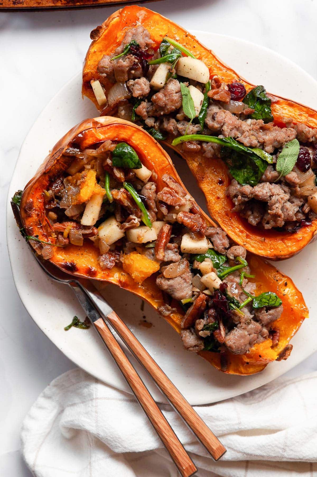 Two stuffed butternut squash halves on white plate with utensils.