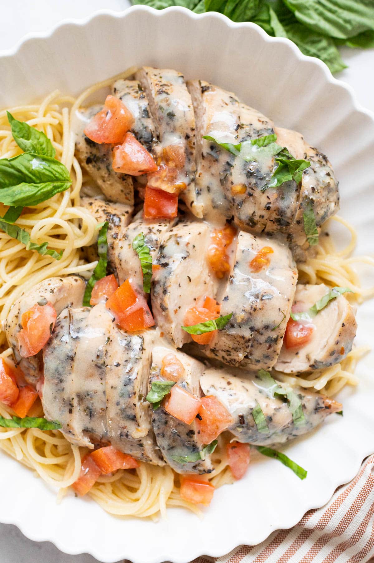 Sliced Italian chicken breasts in a sauce with tomato and basil served over spaghetti.