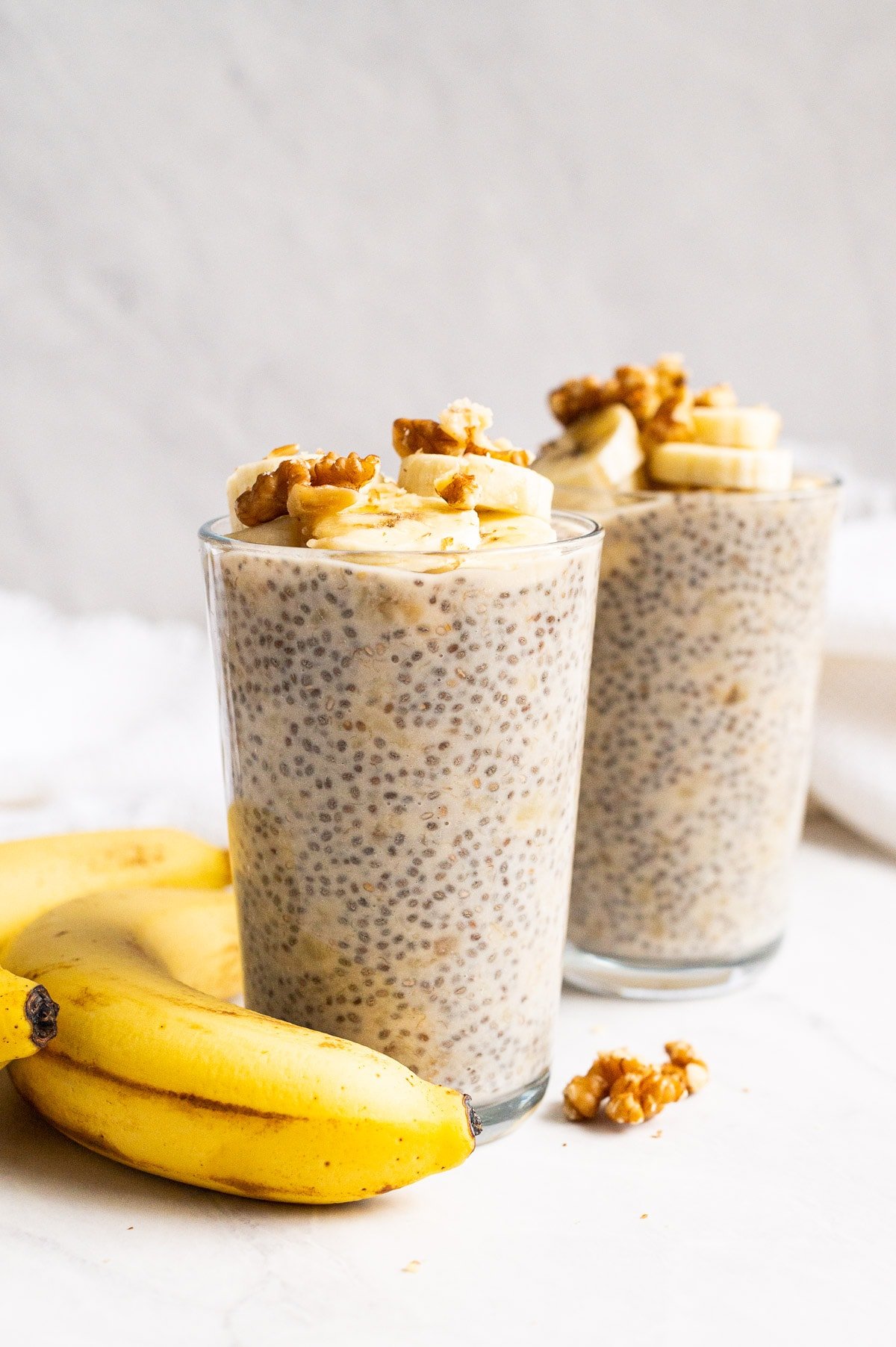 Banana chia pudding topped with sliced bananas and walnuts served in glasses.