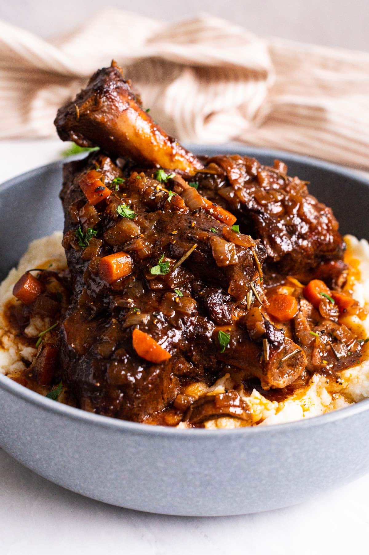 Two braised lamb shanks with gravy stacked on top of mashed potatoes on a plate.