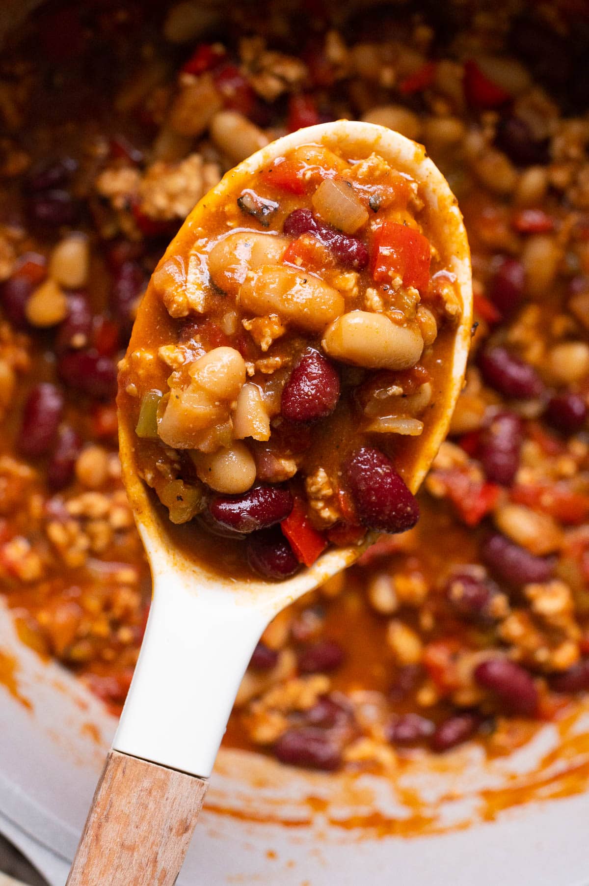 Close up of chicken chili with white beans and red kidney beans on a spoon.