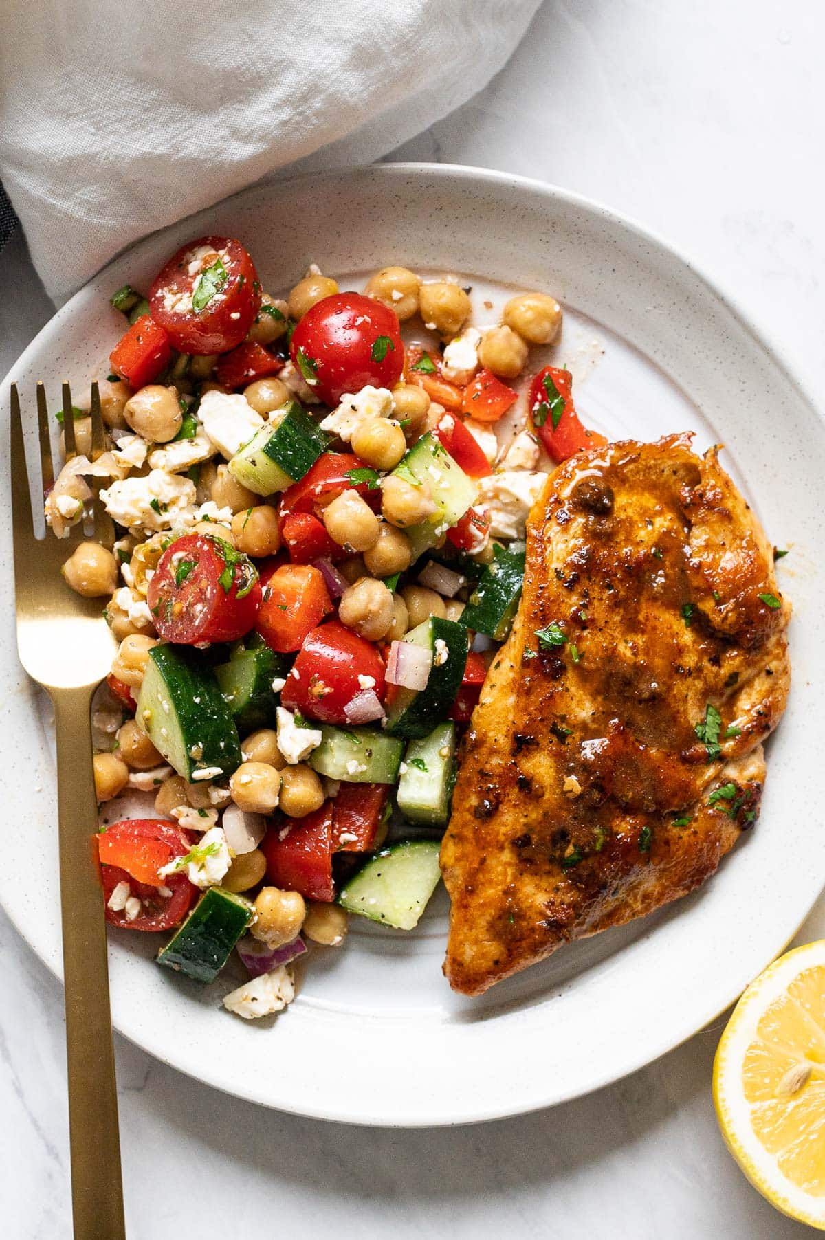Mediterranean chickpea salad served with pan fried chicken breast on a plate with a fork.
