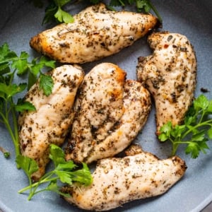 Five chicken breasts with parsley garnish in blue plate.
