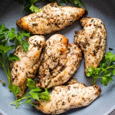 Five chicken breasts with parsley garnish in blue plate.