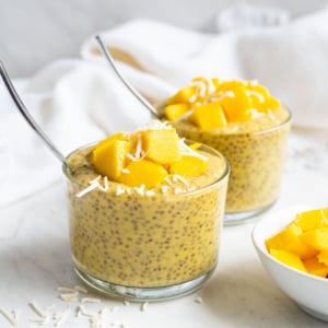 Mango chia pudding in two glasses topped with mango and coconut flakes.