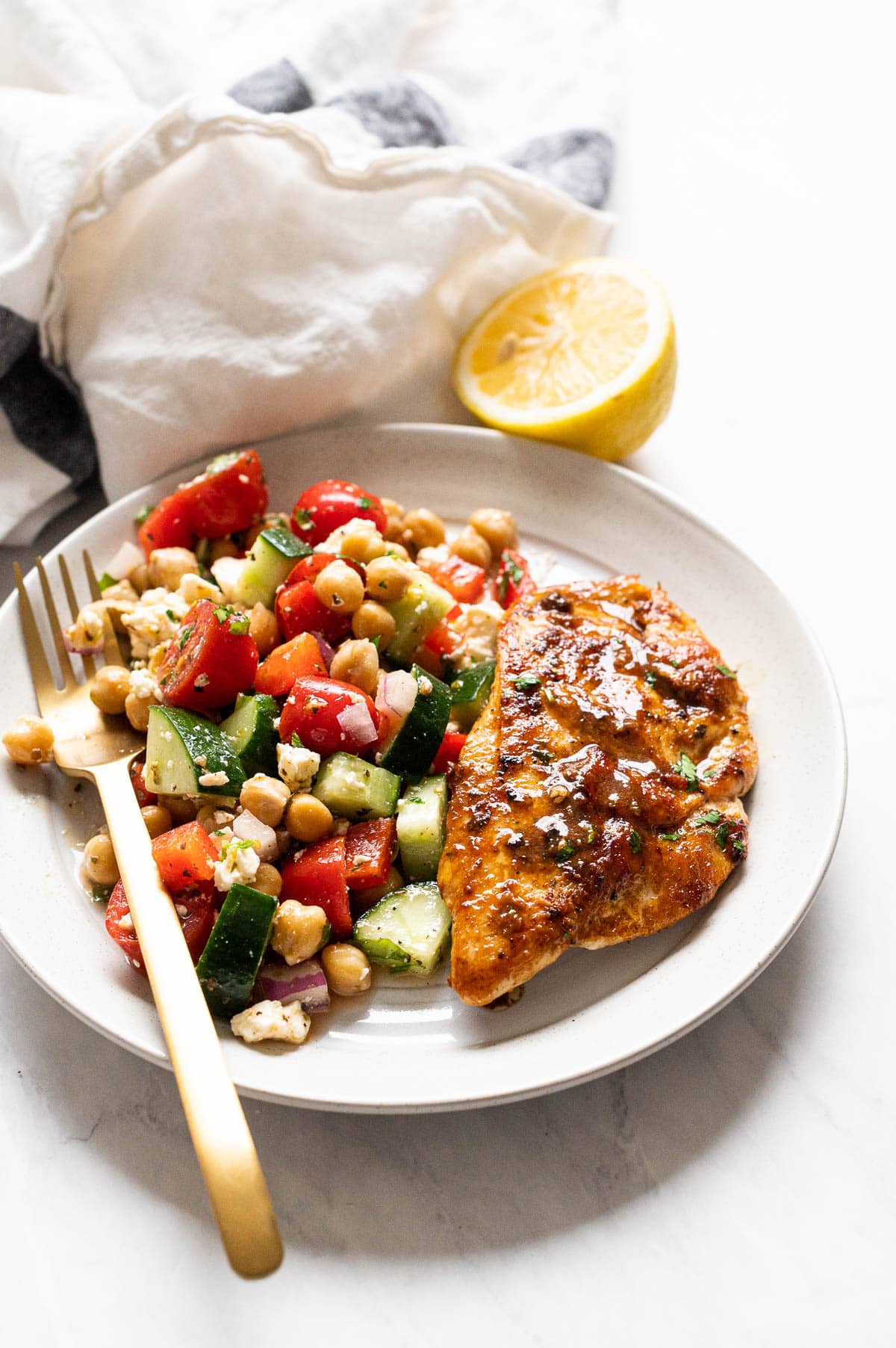 Pan fried chicken breast served with Mediterranean chickpea salad on a plate with a fork.