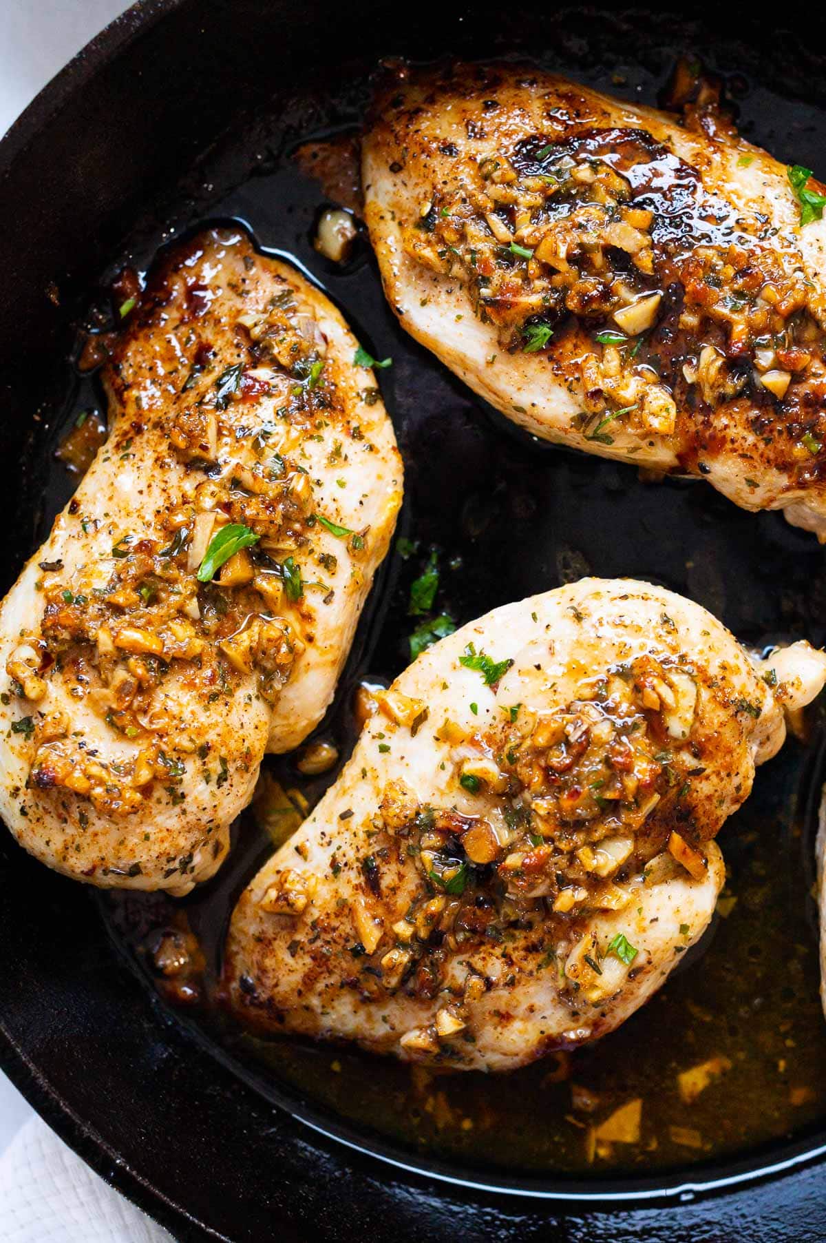 Three cooked chicken breasts with garlic butter sauce in cast iron skillet.