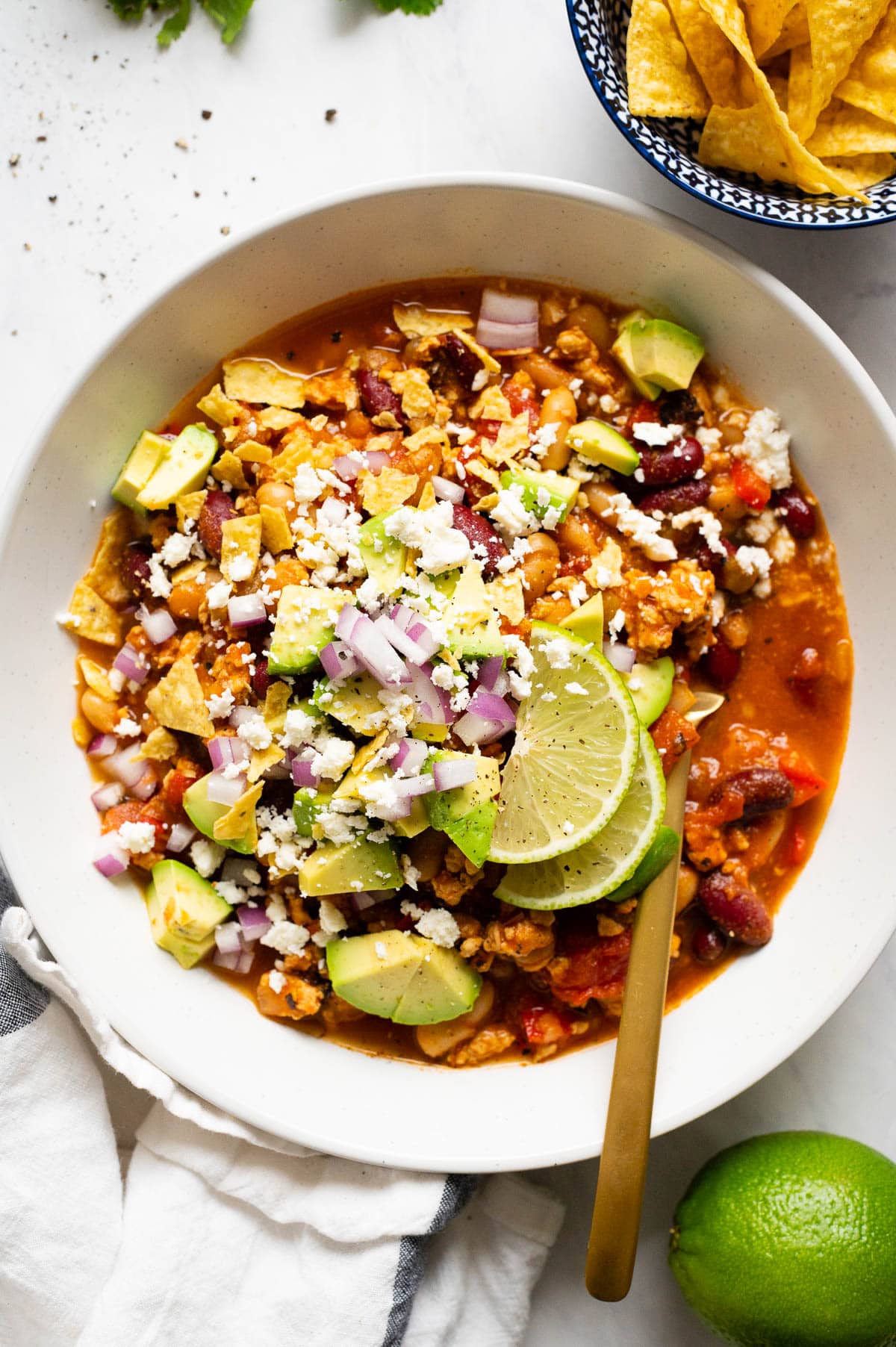 Ground chicken chili with avocado, cheese, red onion and lime served in a bowl.