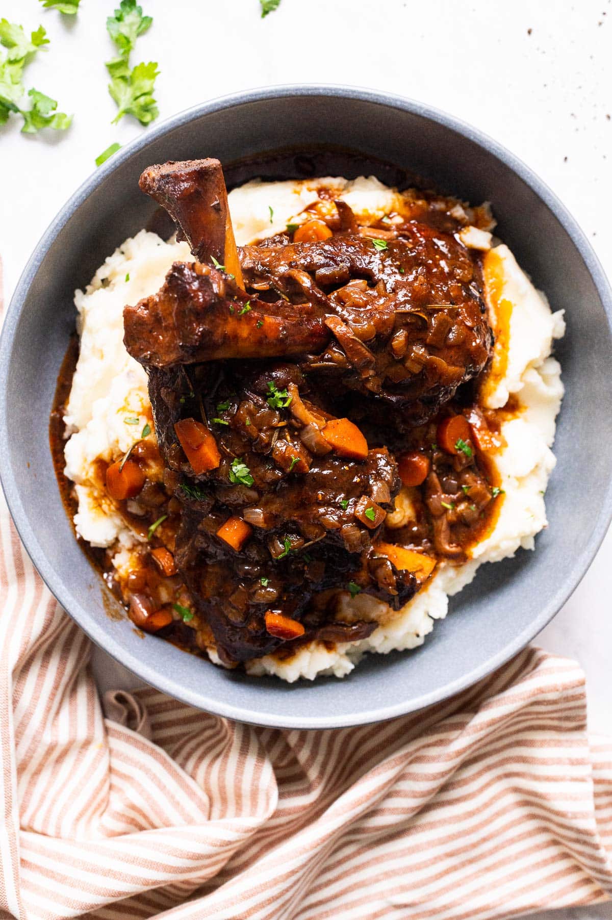 Lamb shanks served over mashed potatoes on blue plate.