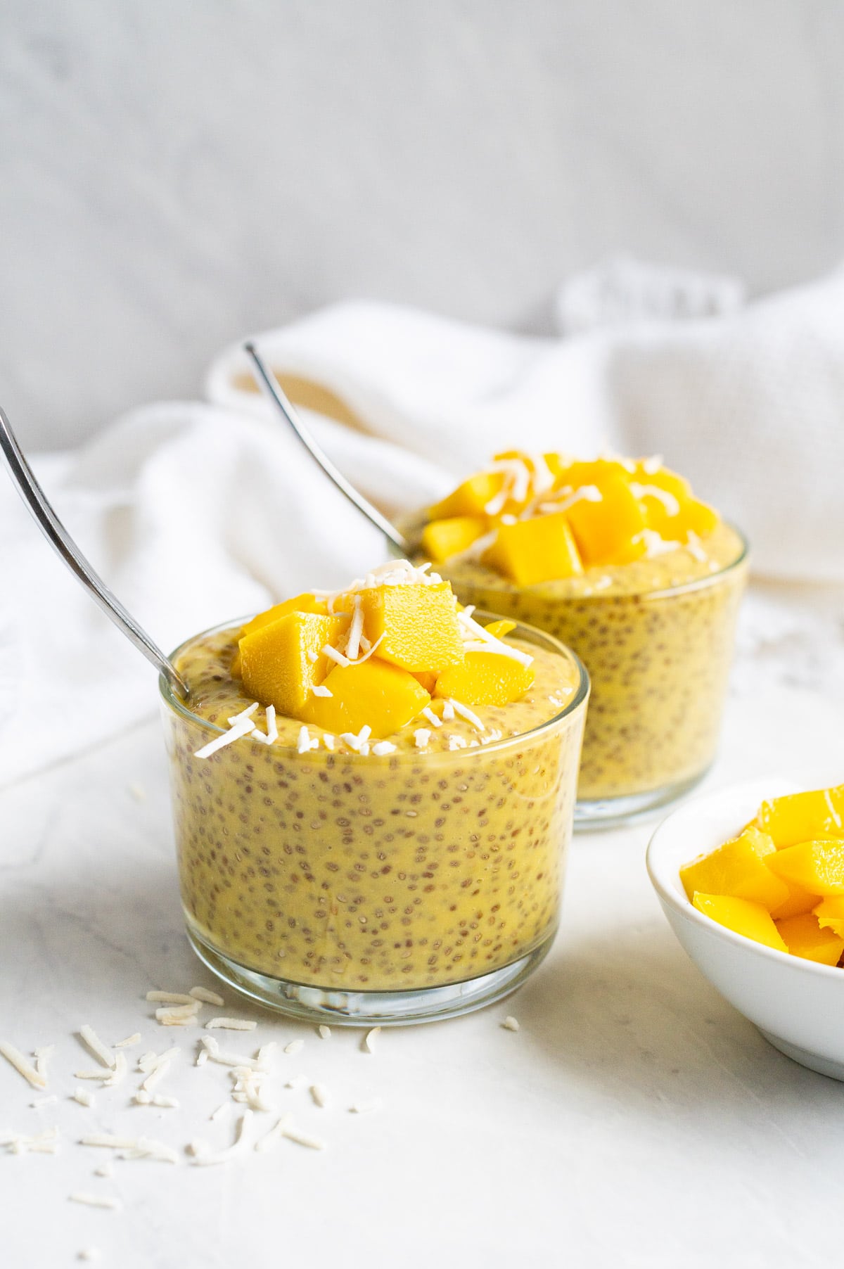 Mango chia pudding in two glasses topped with mango and coconut flakes.