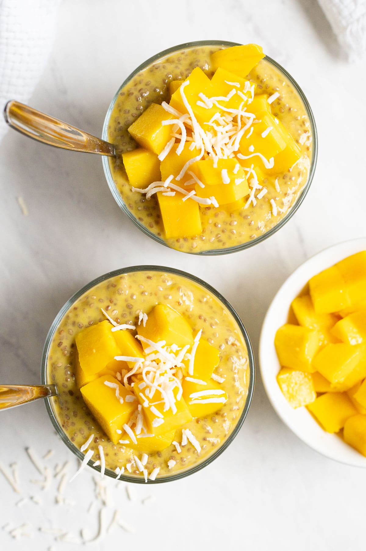 View from the top of mango chia seed pudding in glasses topped with mango and coconut flakes.
