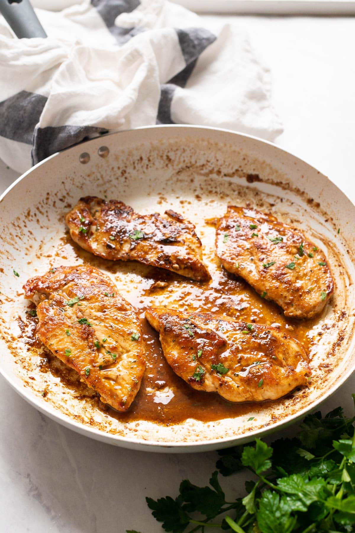 Four fried chicken breasts with sauce and garnished with parsley in a skillet.