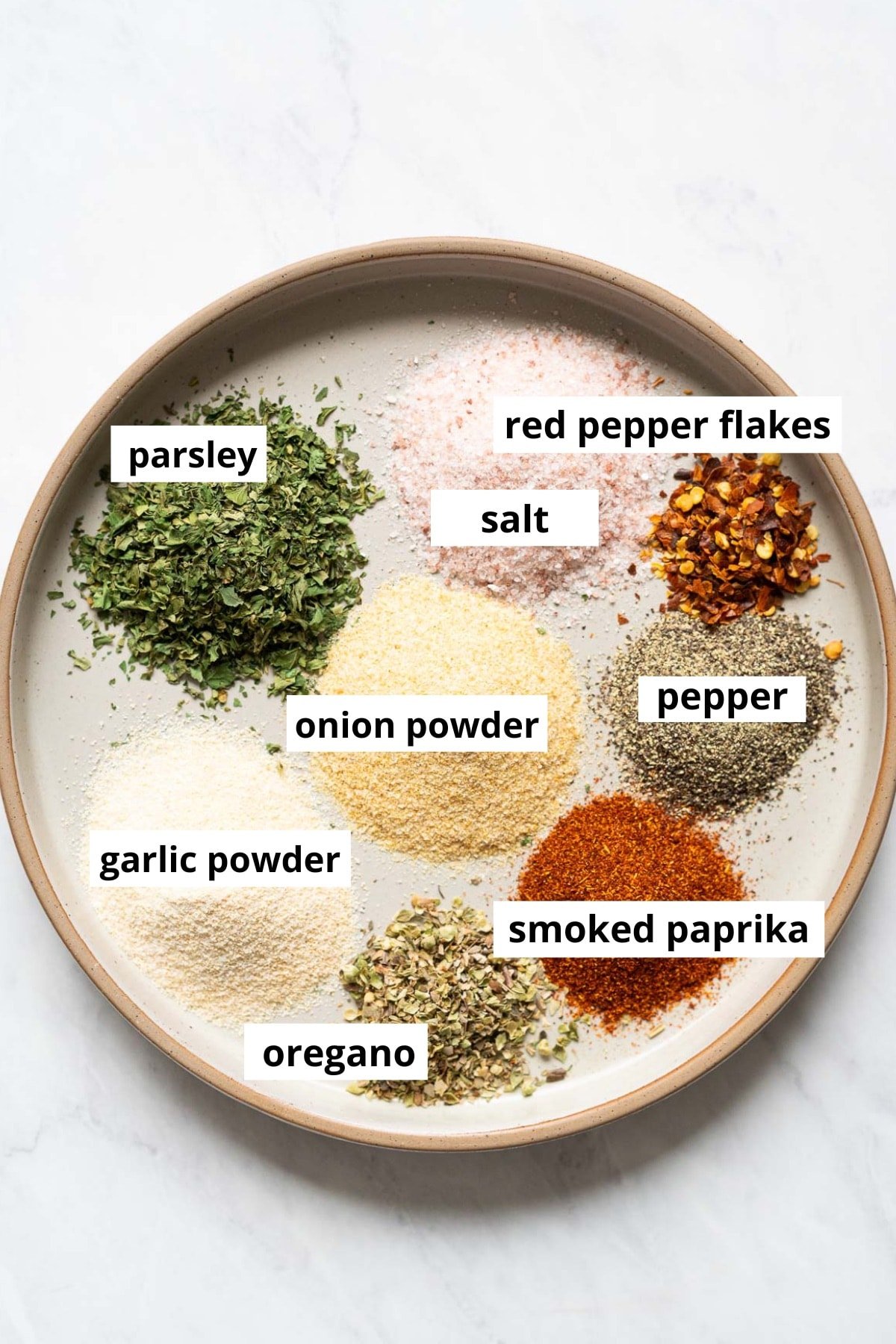 Onion powder, garlic powder, red pepper flakes, parsley, salt, pepper, smoked paprika, garlic powder, oregano on a plate.