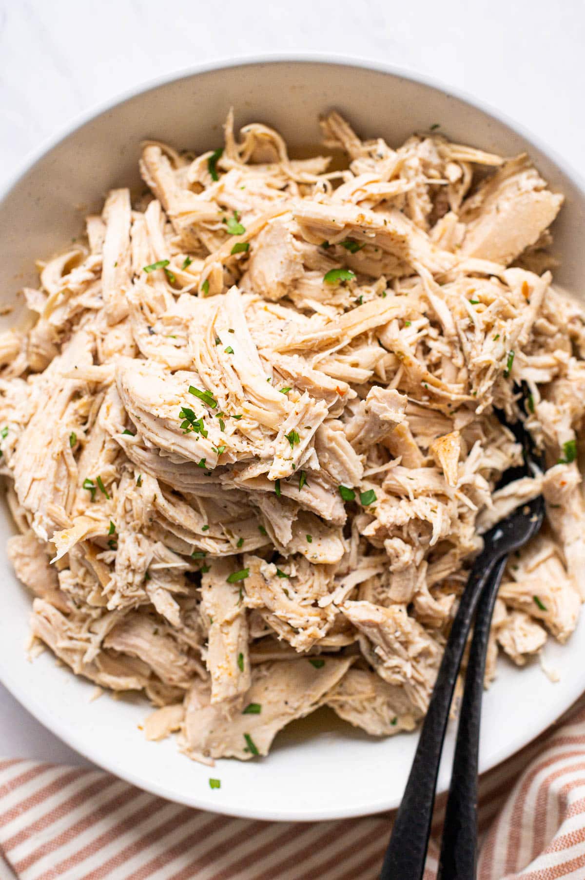 Shredded chicken on a plate with forks garnished with parsley.
