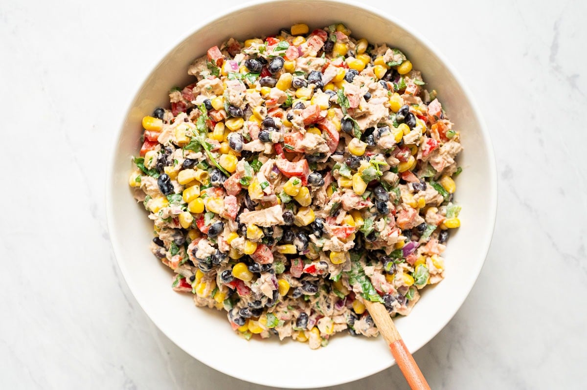 Mexican tuna salad in white bowl with wooden spoon.