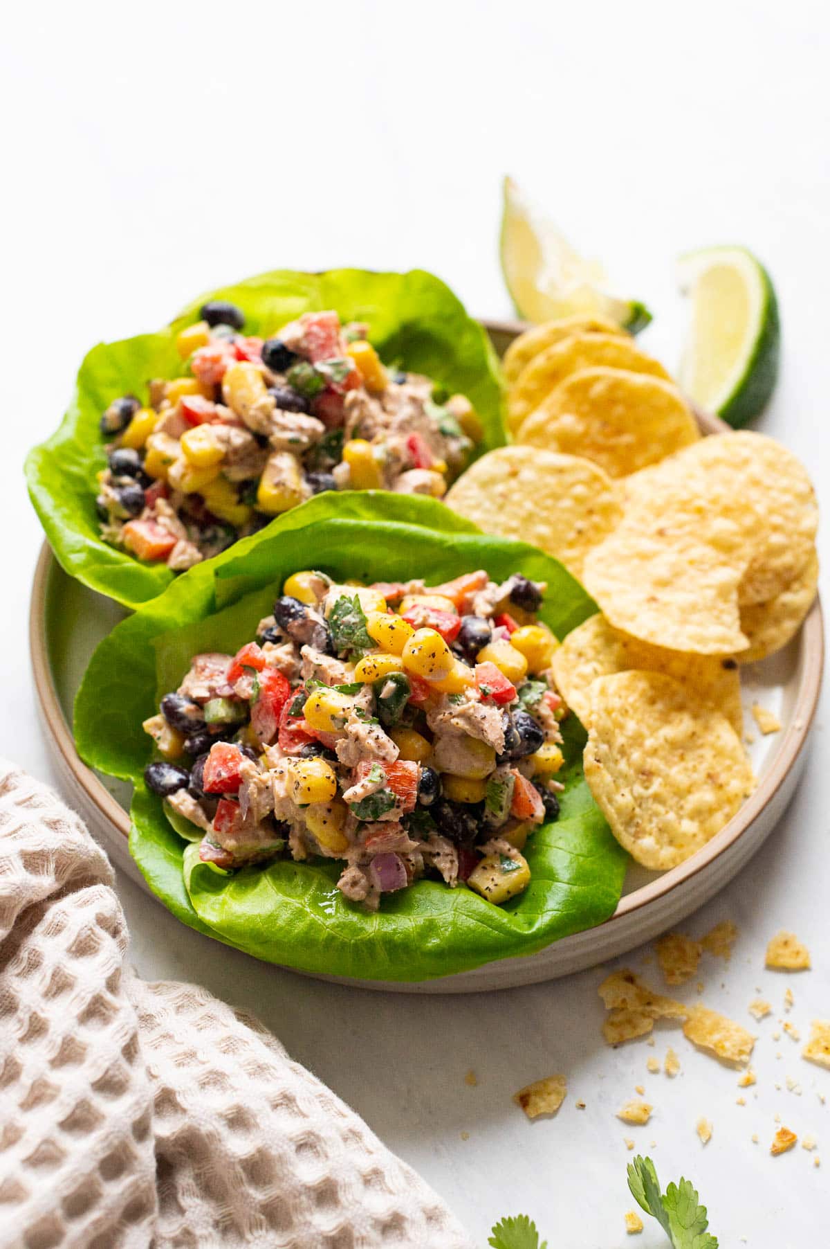 Mexican tuna salad in butter cop leaves with chips on a plate. Towel and lime wedges nearby.