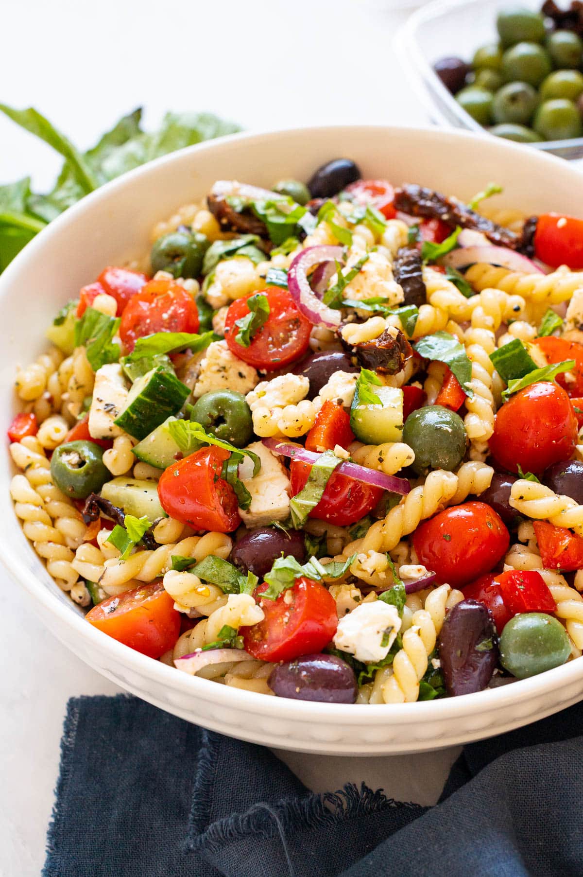 Mediterranean pasta salad with olives, cucumbers, tomatoes and feta cheese in white bowl.