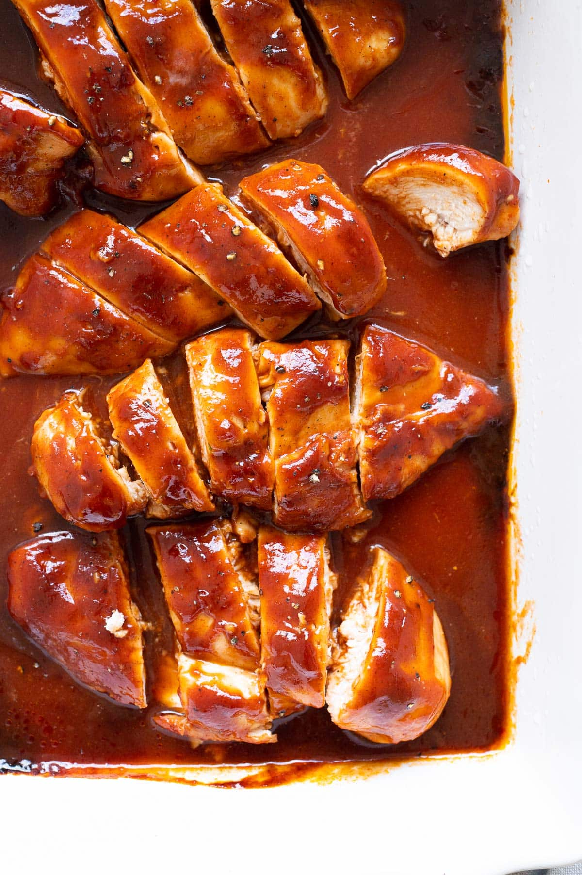 Sliced baked barbecue chicken breasts with sauce in a baking dish.