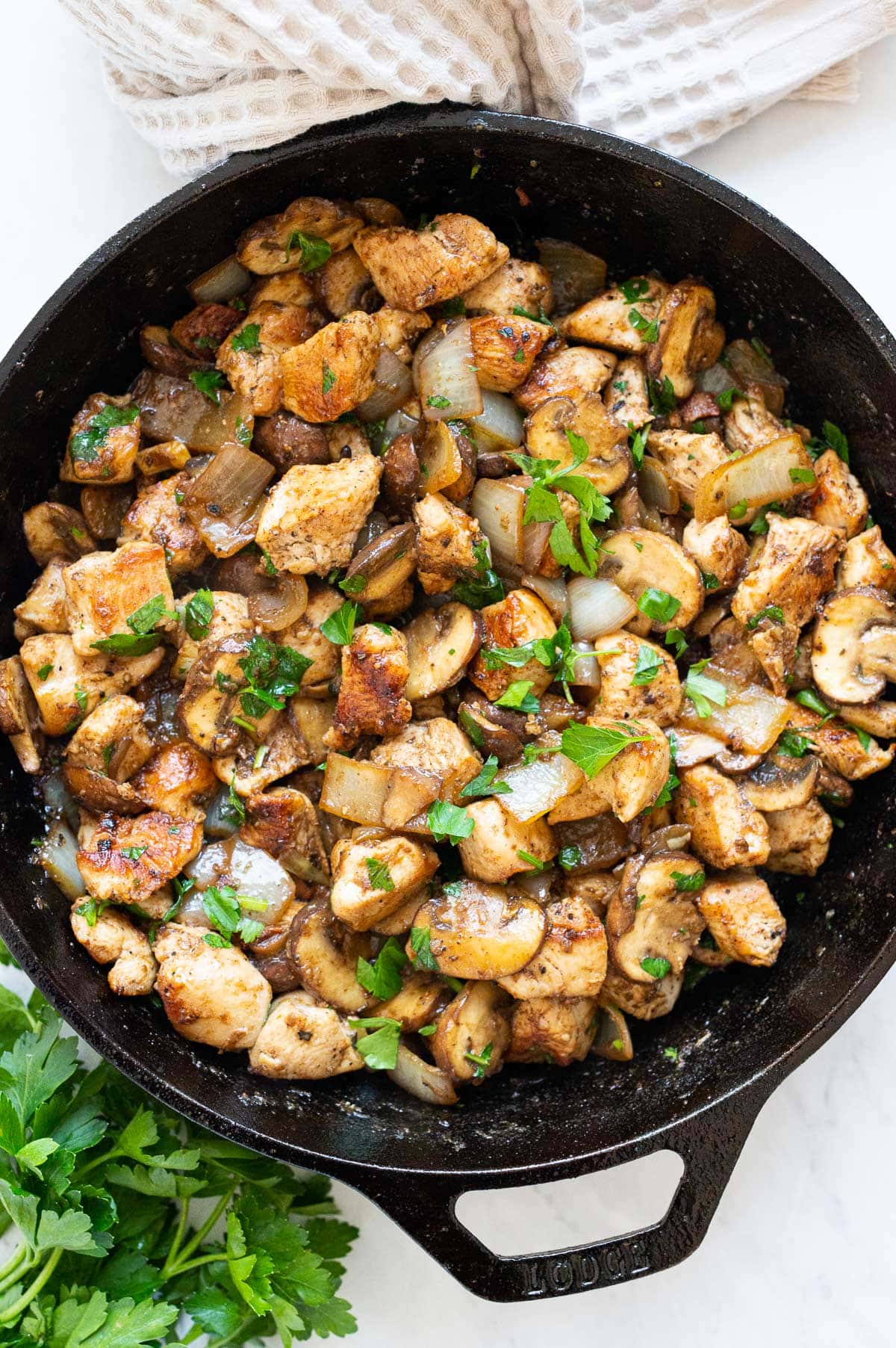 Sauteed chicken and mushrooms garnished with parsley in a skillet.