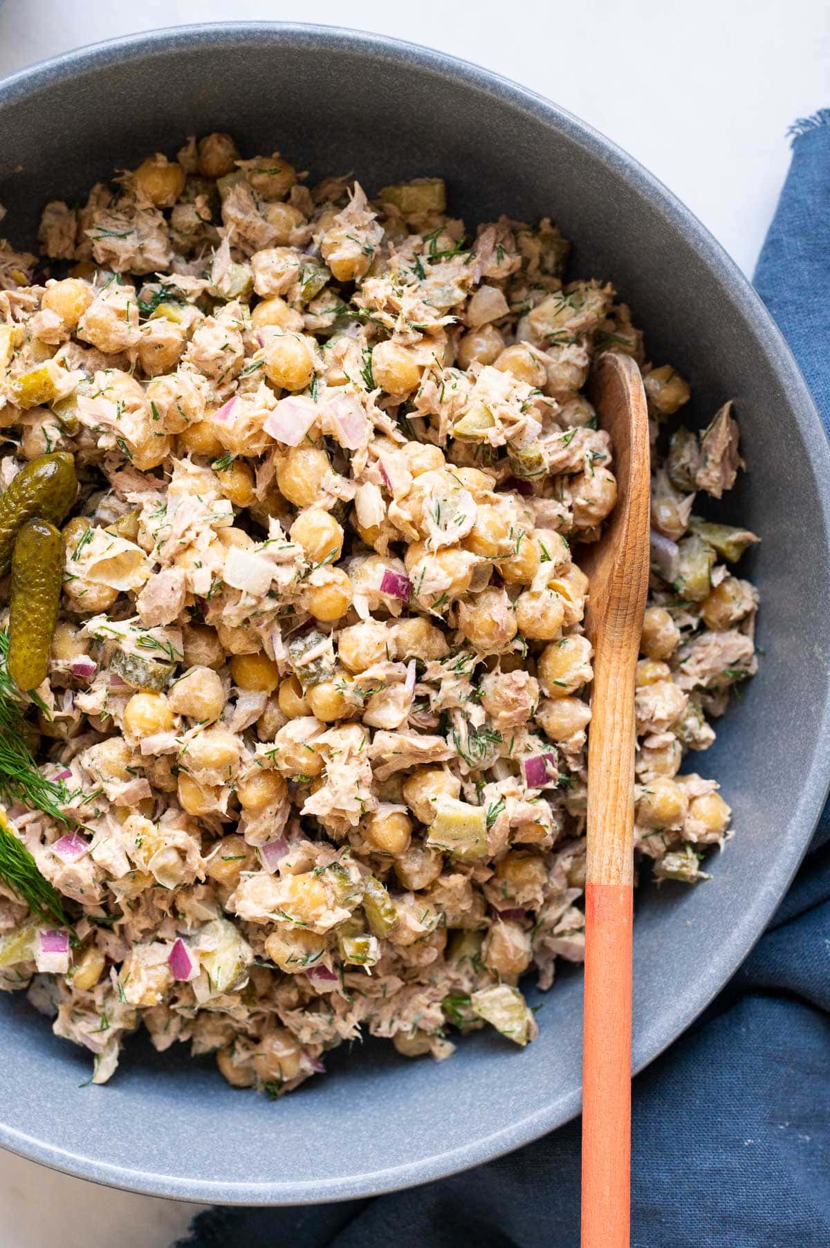 Close up of chickpea tuna salad in blue bowl with a wooden spoon.