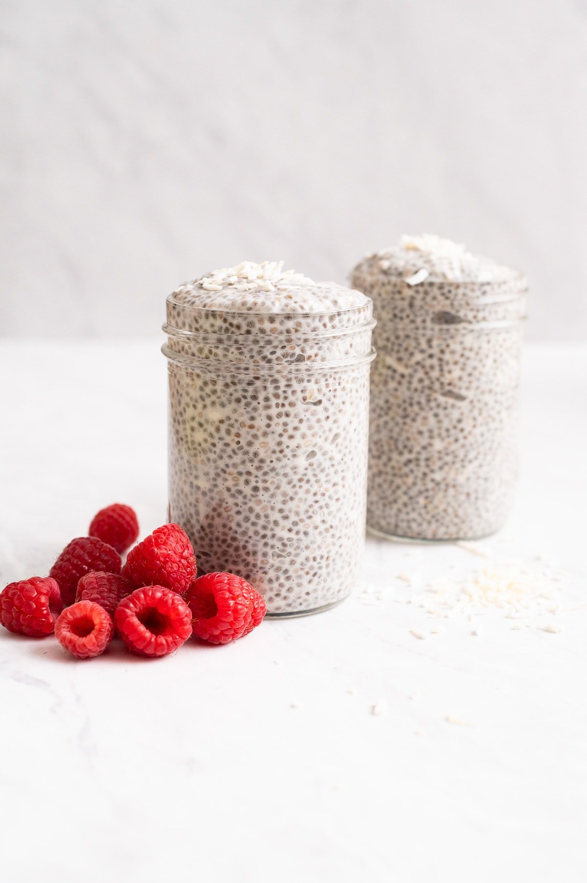Two jars with coconut milk chia pudding and raspberries.