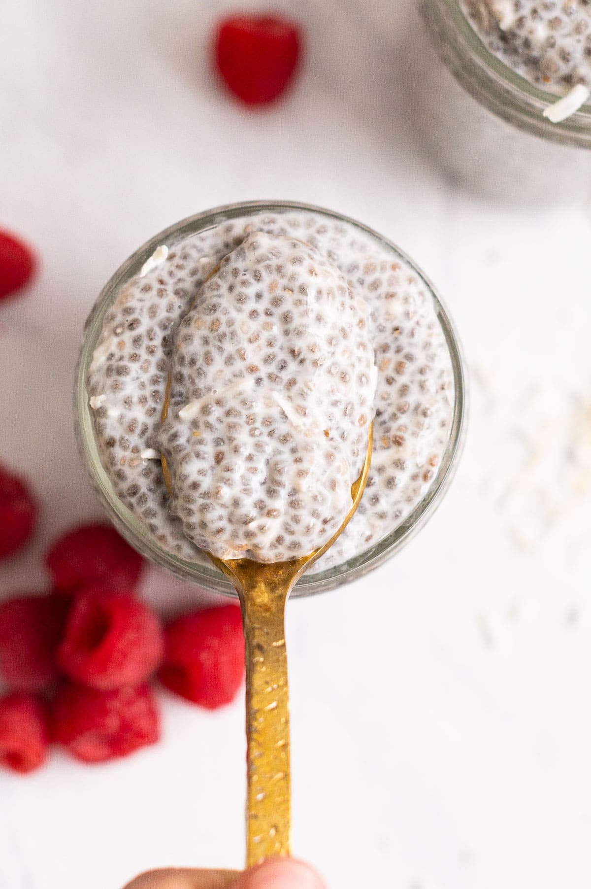Close up of chia pudding showing texture on a golden spoon above the jar.