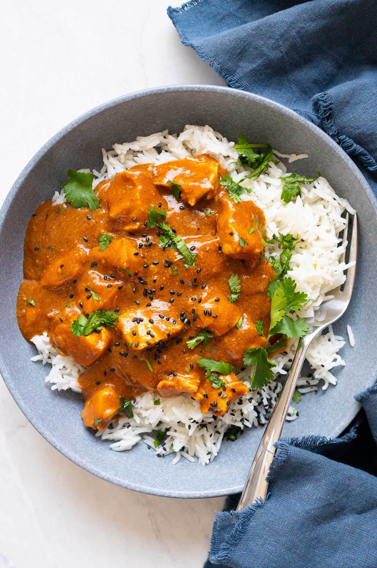 Crock pot butter chicken served over rice and garnished with cilantro and sesame seeds.