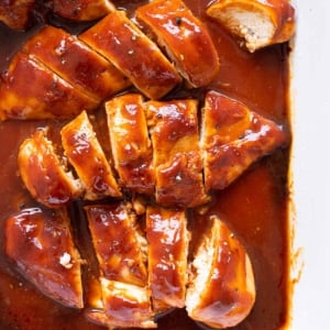 Sliced baked barbecue chicken breasts with sauce in a baking dish.