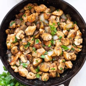 Sauteed chicken and mushrooms garnished with parsley in a skillet.