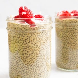 Matcha chia pudding in glass jars garnished with raspberries and coconut flakes.
