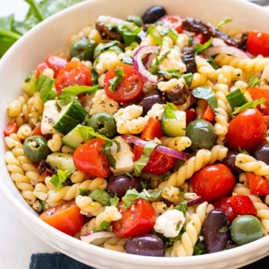 Mediterranean pasta salad with olives, cucumbers, tomatoes and feta cheese in white bowl.