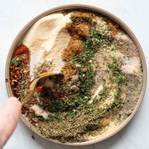 Person stirring spices with a spoon on a plate.