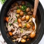 Pot roast with potatoes and carrots in slow cooker with a spoon.