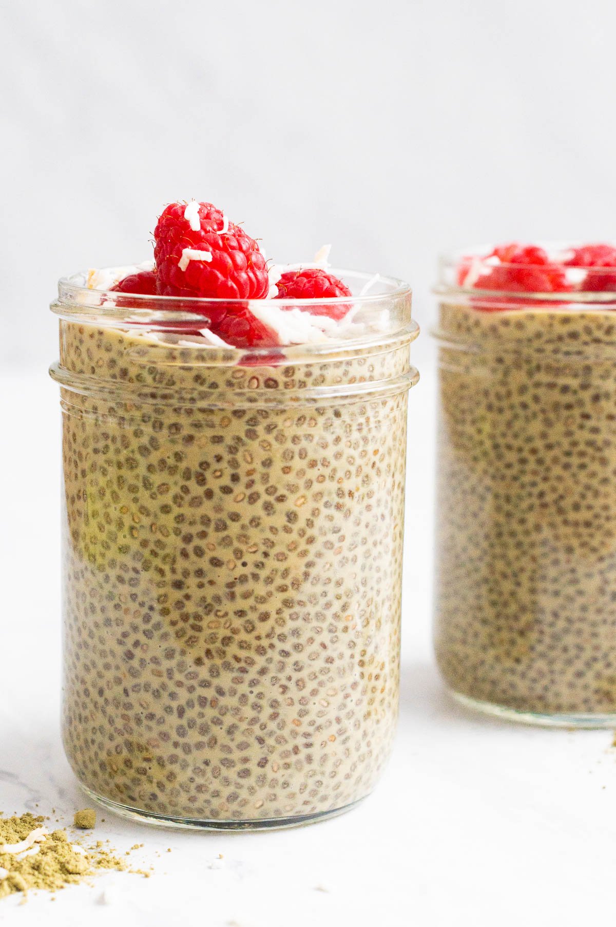 Matcha chia pudding in glass jars garnished with raspberries and coconut flakes.