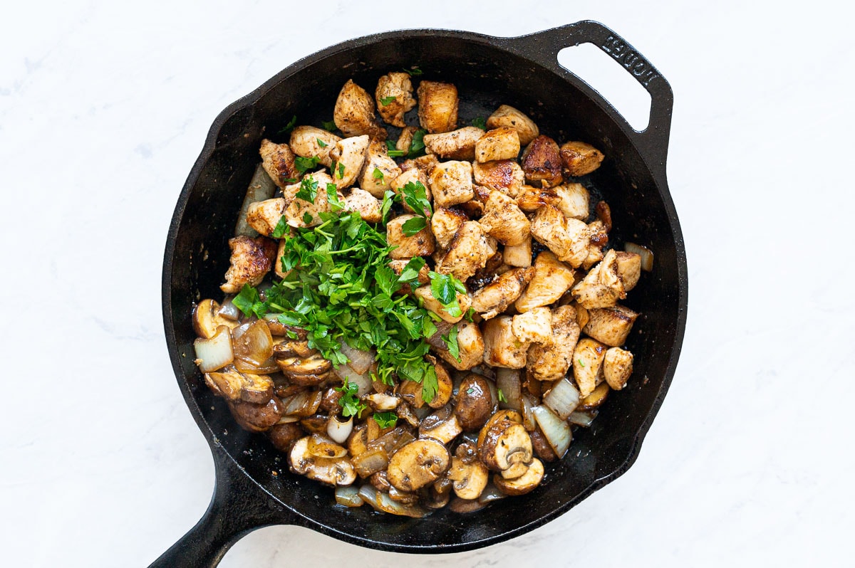 Sauteed mushrooms with onions and chicken and fresh parsley in cast iron skillet.