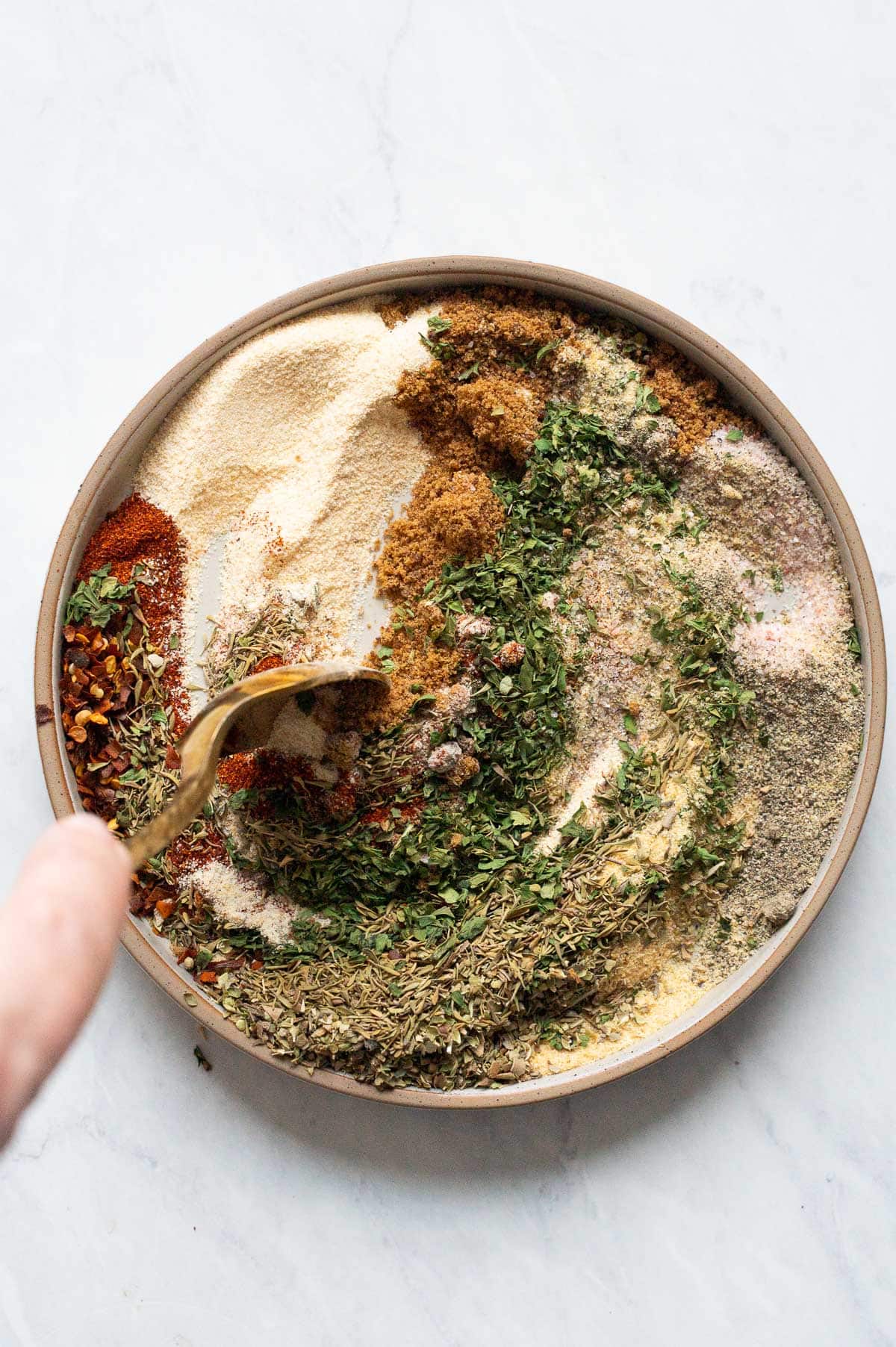 Person stirring spices with a spoon on a plate.