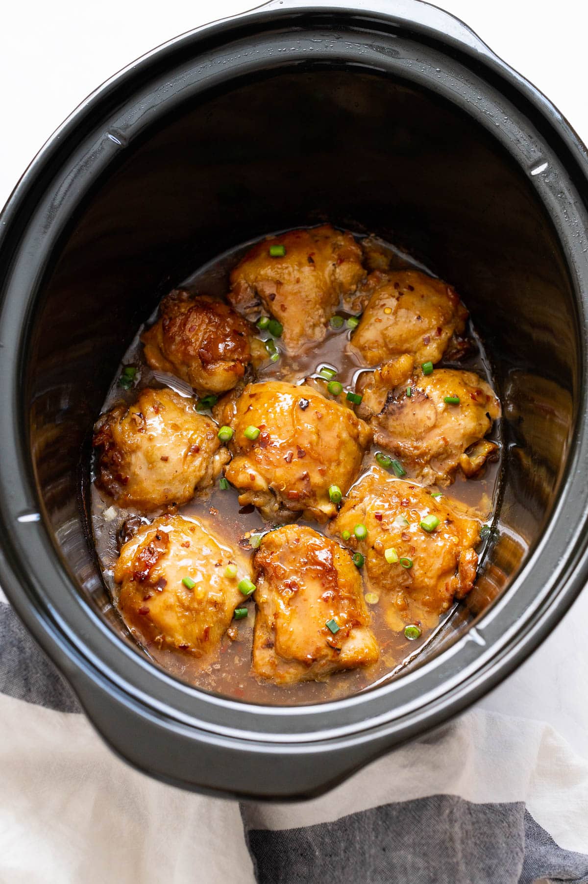 Thai chicken thighs in crock pot garnished with green onions.