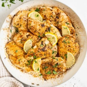 Lemon pepper chicken with sliced lemons and parsley in a skillet.