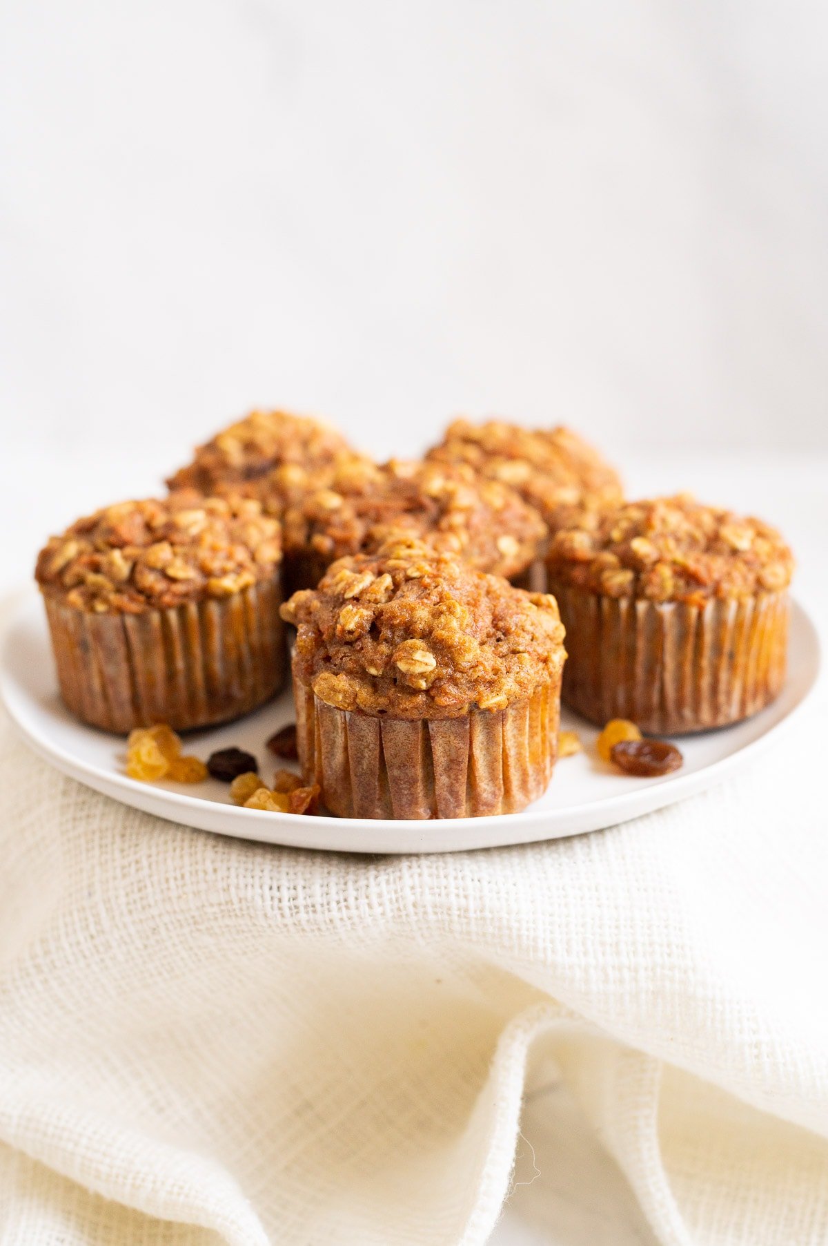 Five healthy carrot cake muffins on white plate with raisins.