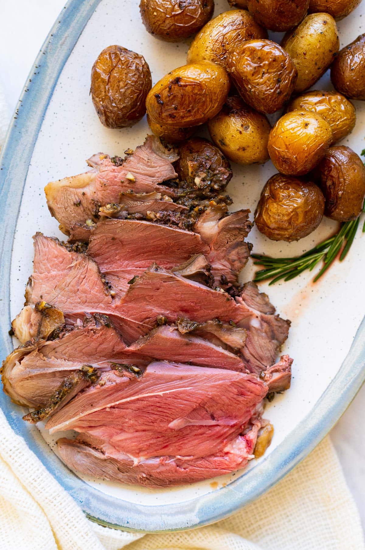 Roasted leg of lamb slices served with baby potatoes on a platter.