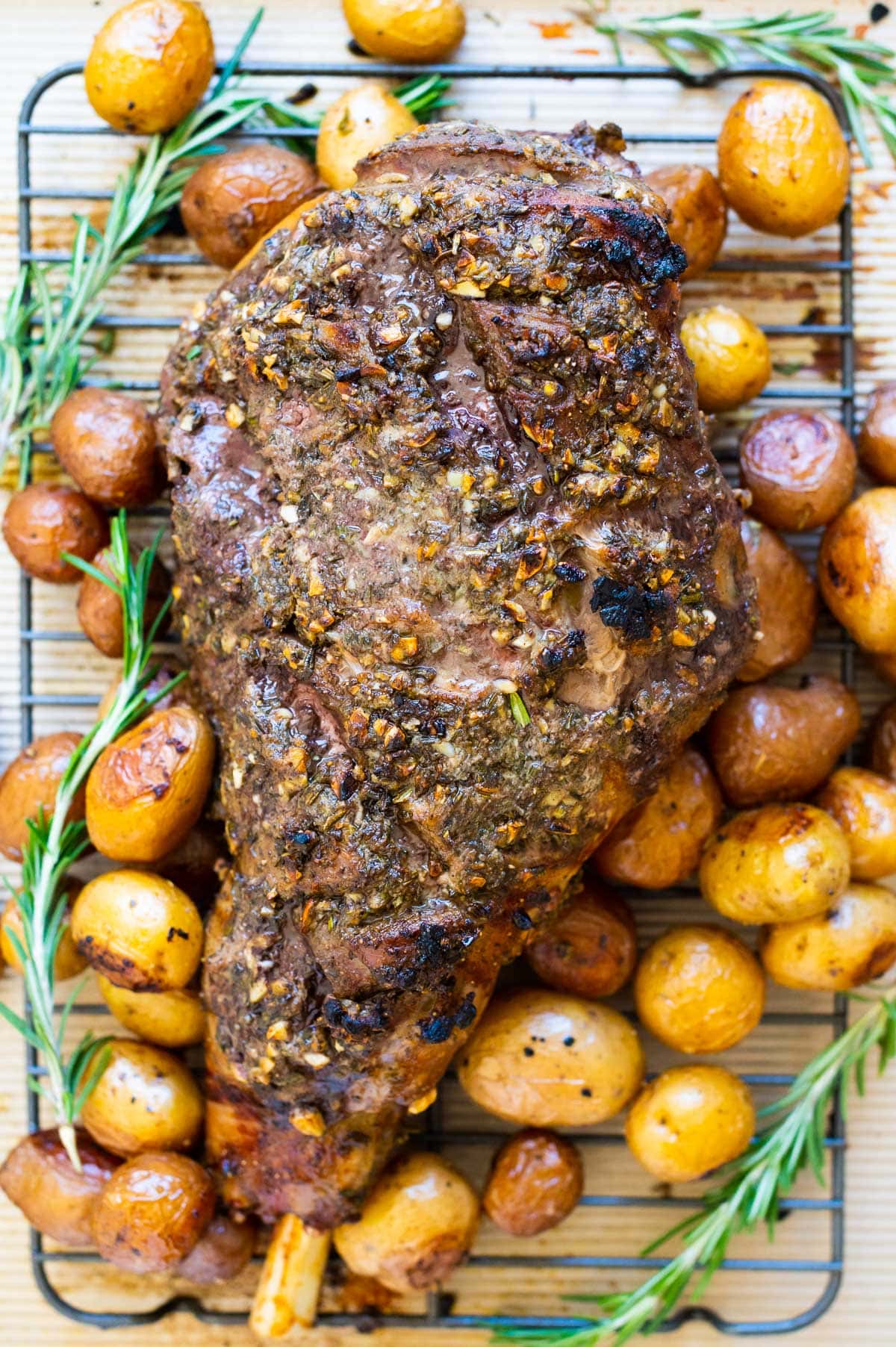 Roasted leg of lamb with baby potatoes and rosemary on a baking tray.