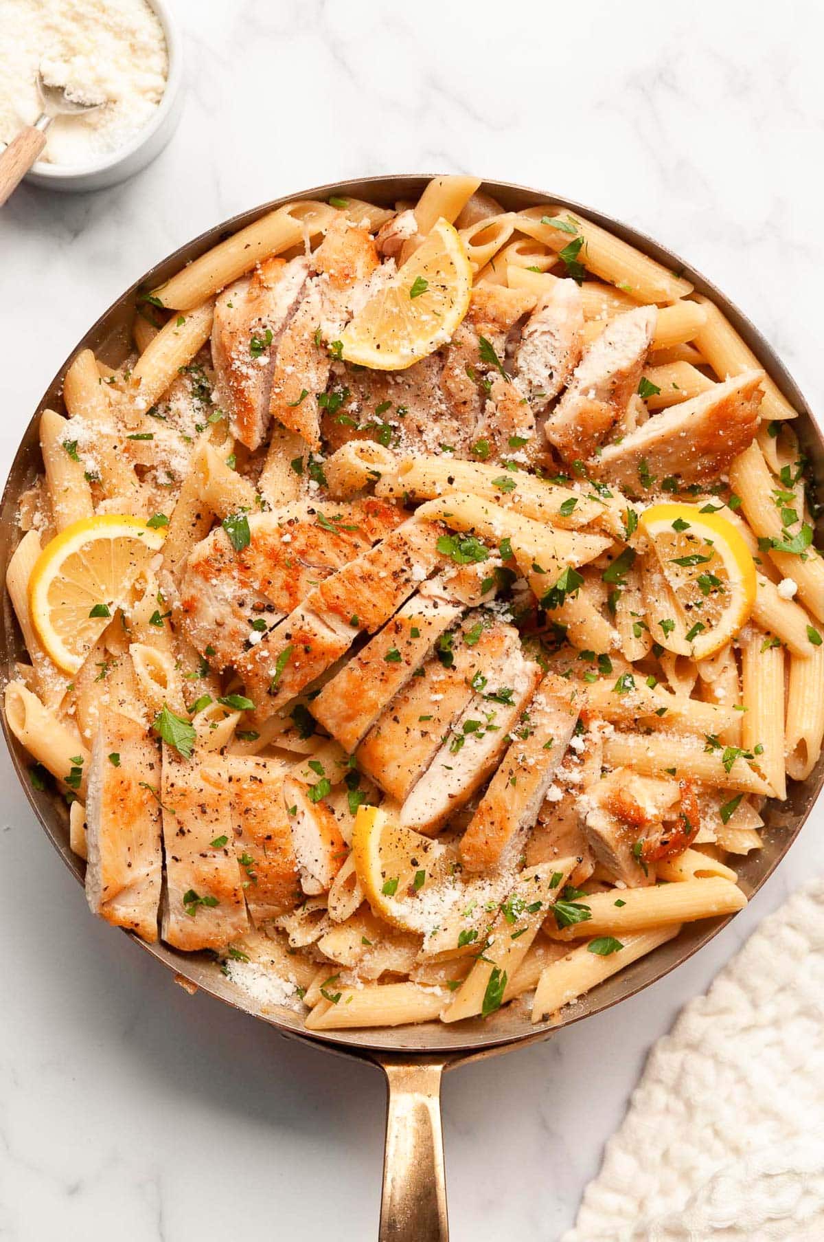 Lemon chicken pasta garnished with Parmesan cheese and parsley in a skillet.