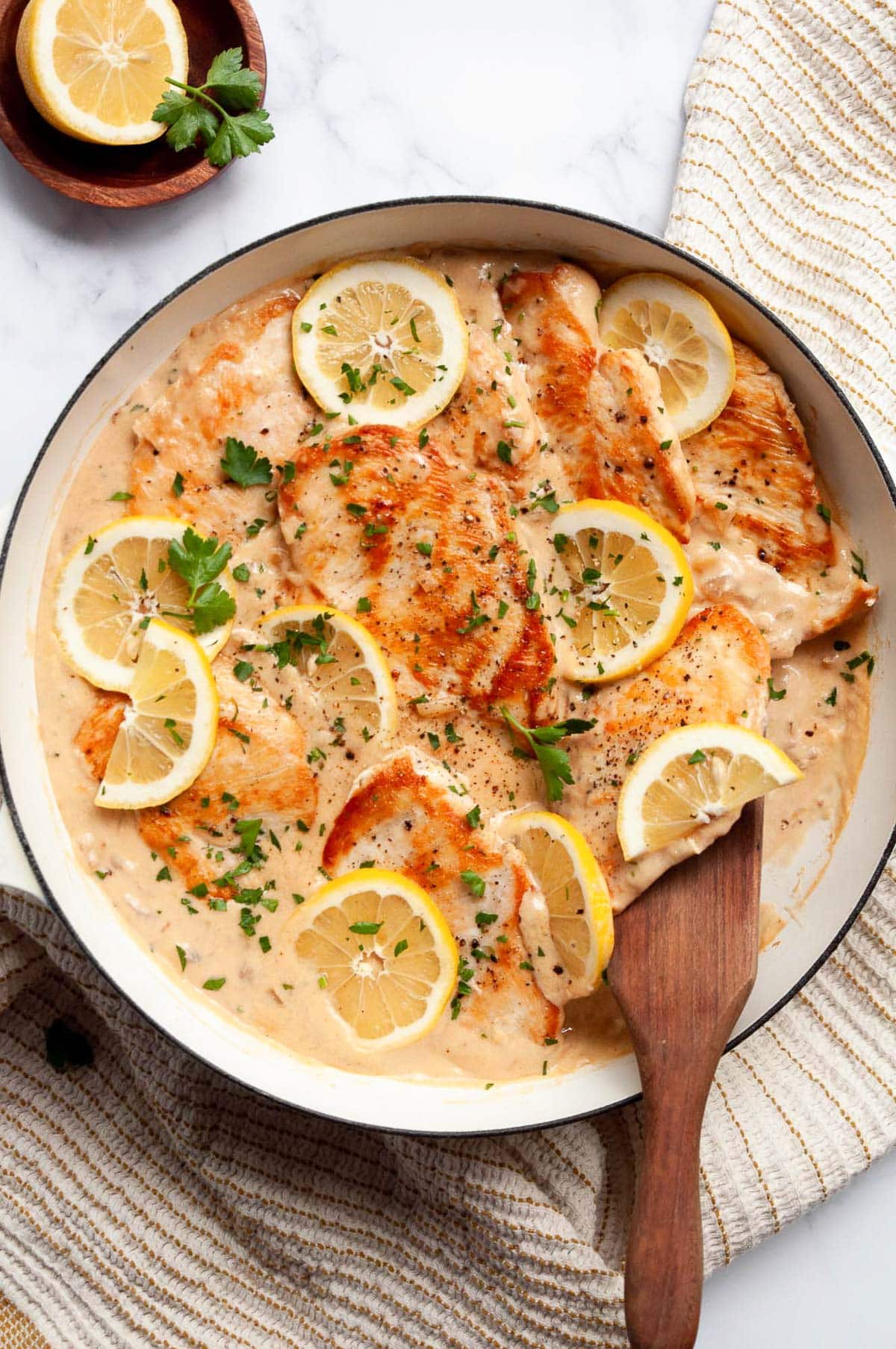 Lemon garlic chicken in creamy sauce served in white skillet with a wooden spoon.