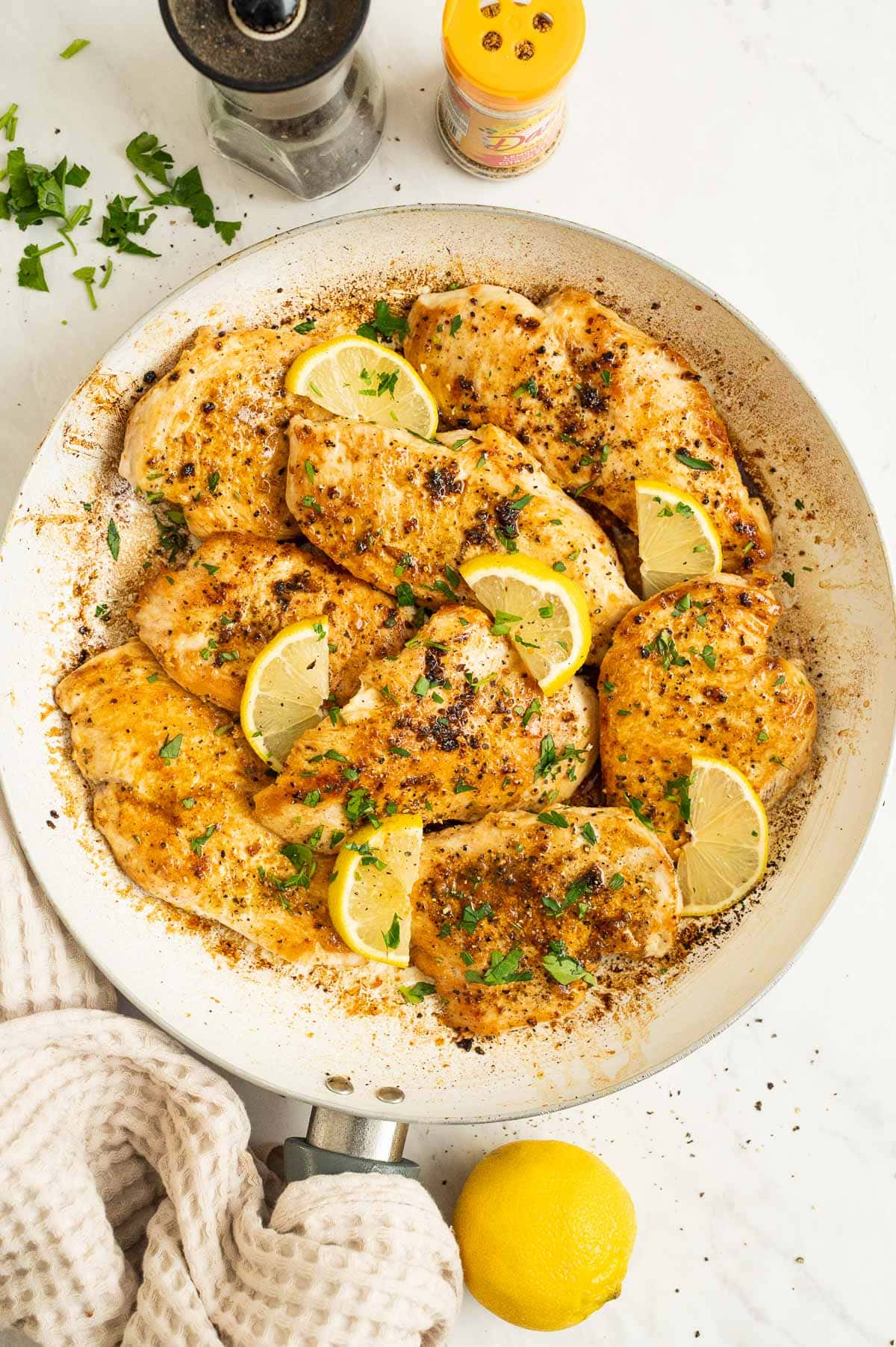 Lemon pepper chicken with sliced lemons and parsley in a skillet.