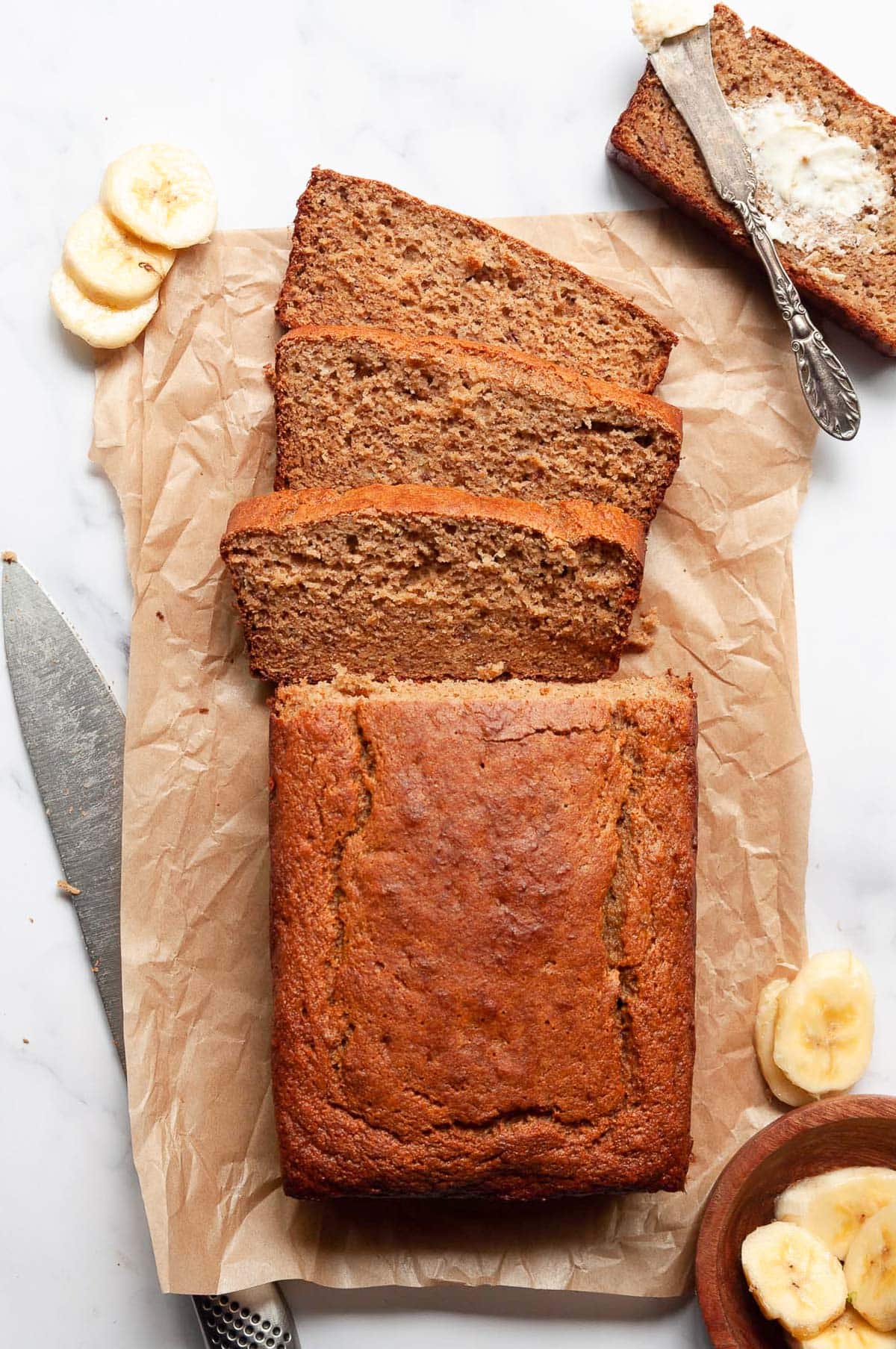 Sliced protein banana bread, banana slices and butter piece of bread on a counter.